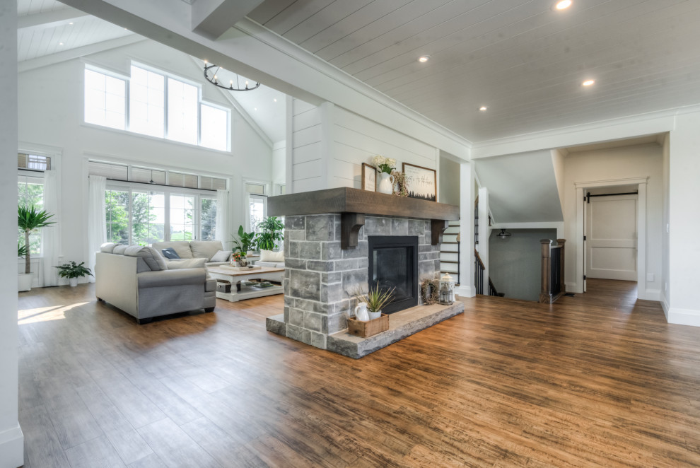 Inspiration for a large country open concept living room in Toronto with white walls, medium hardwood floors, a two-sided fireplace, a stone fireplace surround, a concealed tv, multi-coloured floor and timber.