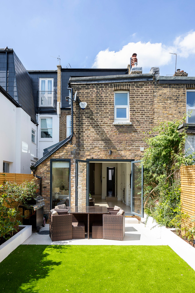 Photo of a mid-sized contemporary two-storey brick brown townhouse exterior in London with a flat roof and a metal roof.