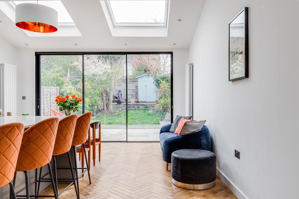 Design ideas for a large contemporary eat-in kitchen in London with a drop-in sink, grey cabinets, quartzite benchtops, orange splashback, glass sheet splashback, coloured appliances, light hardwood floors, brown floor, white benchtop and vaulted.