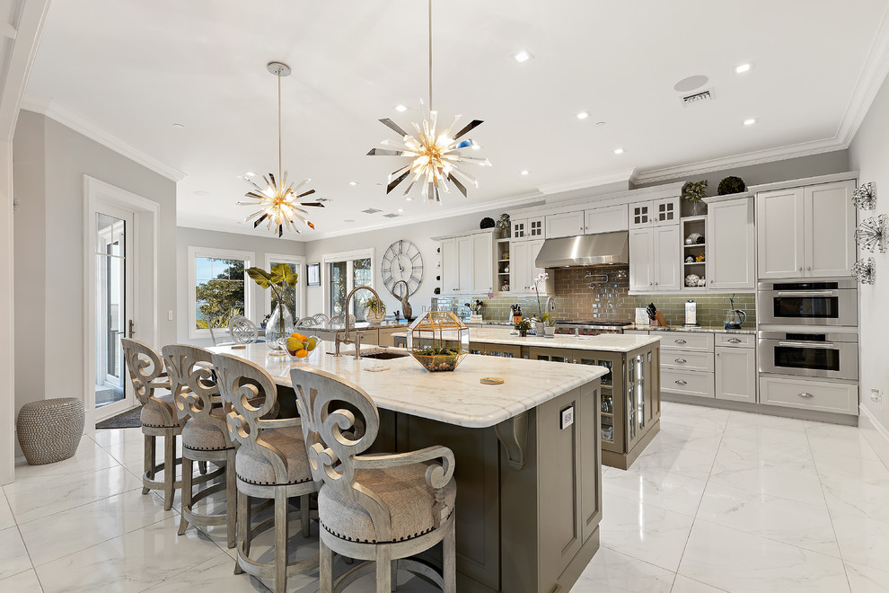This is an example of a beach style l-shaped eat-in kitchen in Tampa with an undermount sink, shaker cabinets, white cabinets, grey splashback, subway tile splashback, stainless steel appliances, multiple islands, white floor and white benchtop.