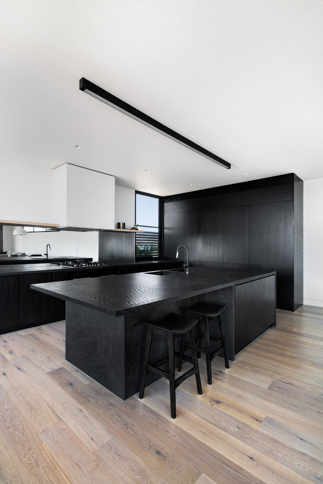 Inspiration for a contemporary l-shaped kitchen in Melbourne with an undermount sink, flat-panel cabinets, black cabinets, mirror splashback, light hardwood floors, with island, beige floor and black benchtop.