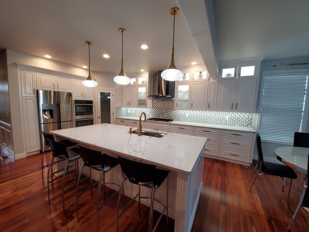 Photo of a large transitional l-shaped eat-in kitchen in Seattle with an undermount sink, raised-panel cabinets, white cabinets, quartz benchtops, multi-coloured splashback, glass tile splashback, stainless steel appliances, medium hardwood floors, with island and white benchtop.