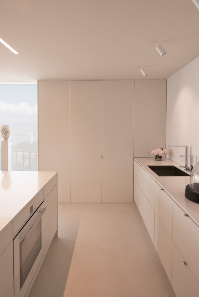 Photo of a small modern single-wall eat-in kitchen in San Francisco with an undermount sink, flat-panel cabinets, white cabinets, quartz benchtops, white splashback, stone slab splashback, white appliances, concrete floors and with island.