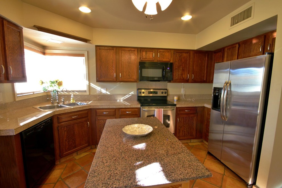 Photo of a small mediterranean l-shaped separate kitchen in Phoenix with a drop-in sink, recessed-panel cabinets, dark wood cabinets, granite benchtops, stainless steel appliances, terra-cotta floors and no island.