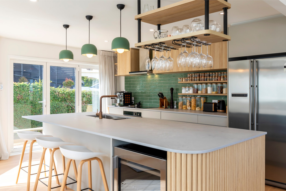 Zweizeilige Moderne Küche mit Unterbauwaschbecken, flächenbündigen Schrankfronten, beigen Schränken, Küchenrückwand in Grün, Rückwand aus Metrofliesen, Küchengeräten aus Edelstahl, hellem Holzboden, Kücheninsel und beigem Boden in Auckland