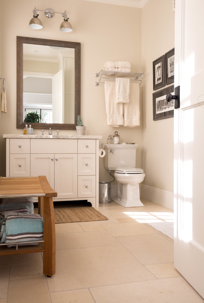 Inspiration for a mid-sized transitional 3/4 bathroom in San Diego with furniture-like cabinets, distressed cabinets, an alcove shower, a two-piece toilet, beige tile, ceramic tile, beige walls, limestone floors, an undermount sink and marble benchtops.