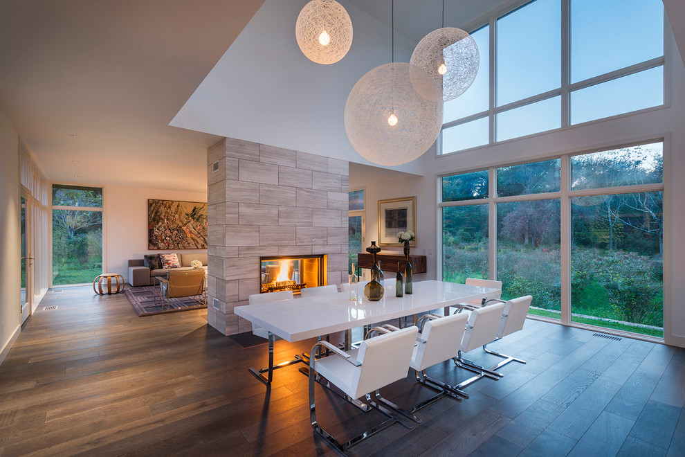 Inspiration for a large contemporary open plan dining in Boston with white walls, dark hardwood floors, a two-sided fireplace and a tile fireplace surround.