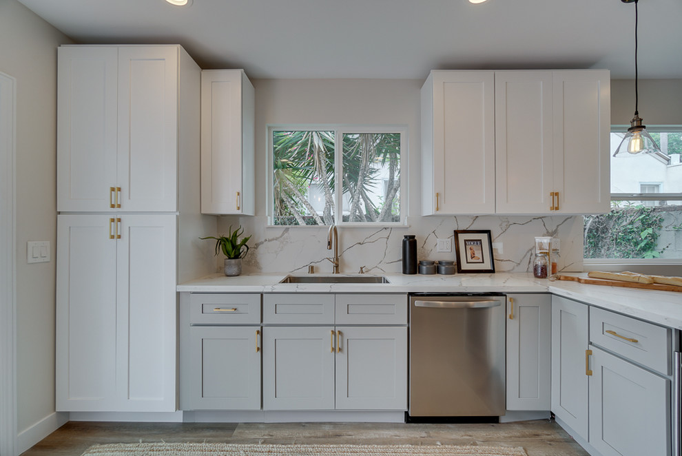 Mid-sized transitional l-shaped eat-in kitchen in Los Angeles with a drop-in sink, shaker cabinets, grey cabinets, quartzite benchtops, white splashback, stone tile splashback, stainless steel appliances, laminate floors, a peninsula and white benchtop.