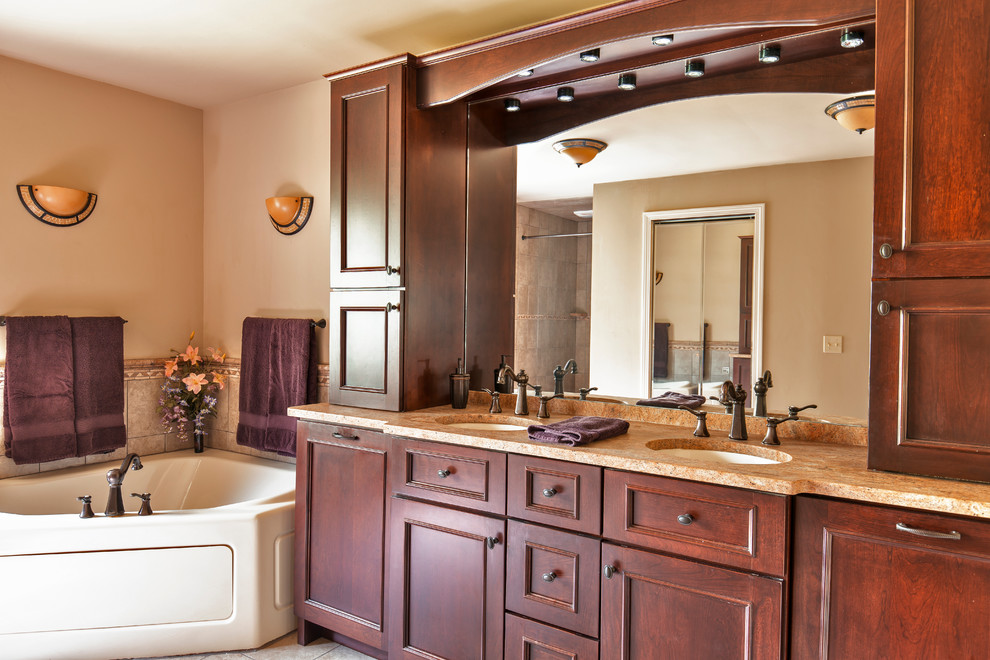 Photo of a mid-sized eclectic master bathroom in Burlington with flat-panel cabinets, medium wood cabinets, granite benchtops, beige tile, an undermount sink, a corner tub, a two-piece toilet, porcelain tile, grey walls and porcelain floors.