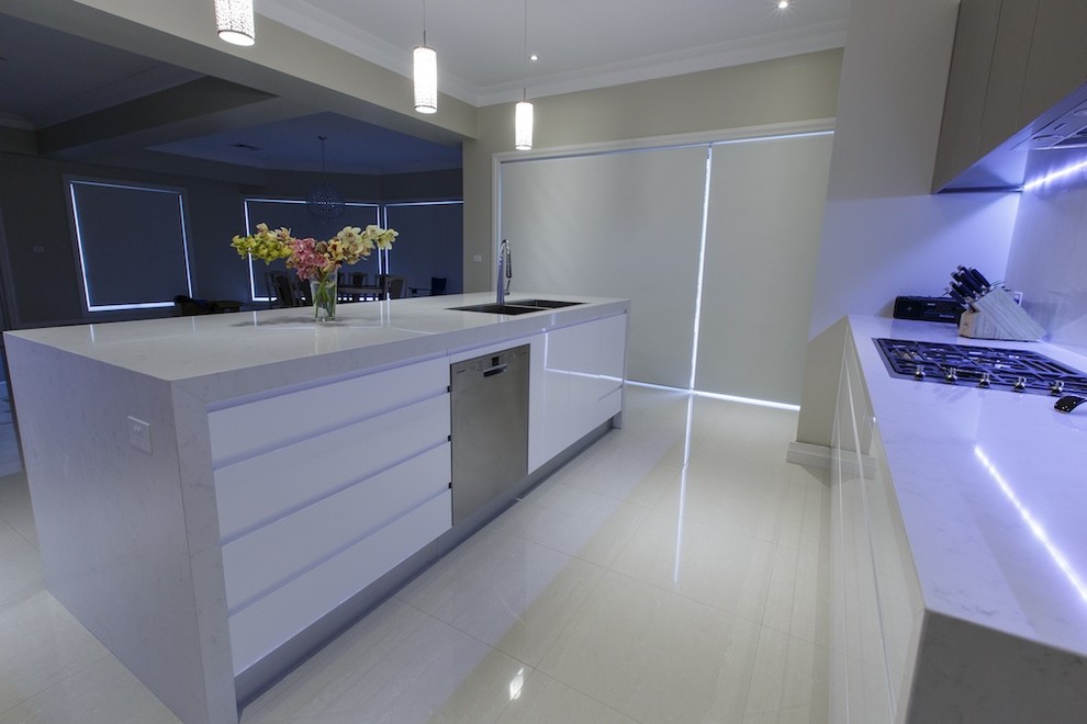 This is an example of a large modern l-shaped open plan kitchen in Sydney with a drop-in sink, flat-panel cabinets, white cabinets, quartz benchtops, white splashback, glass sheet splashback, stainless steel appliances, ceramic floors and with island.