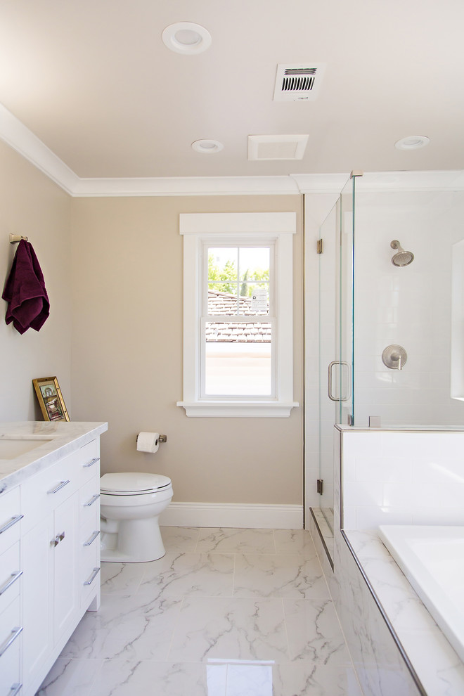 Photo of a large transitional master bathroom in San Francisco with flat-panel cabinets, white cabinets, a corner shower, a two-piece toilet, white tile, porcelain tile, beige walls, porcelain floors, an undermount sink, marble benchtops, white floor and white benchtops.