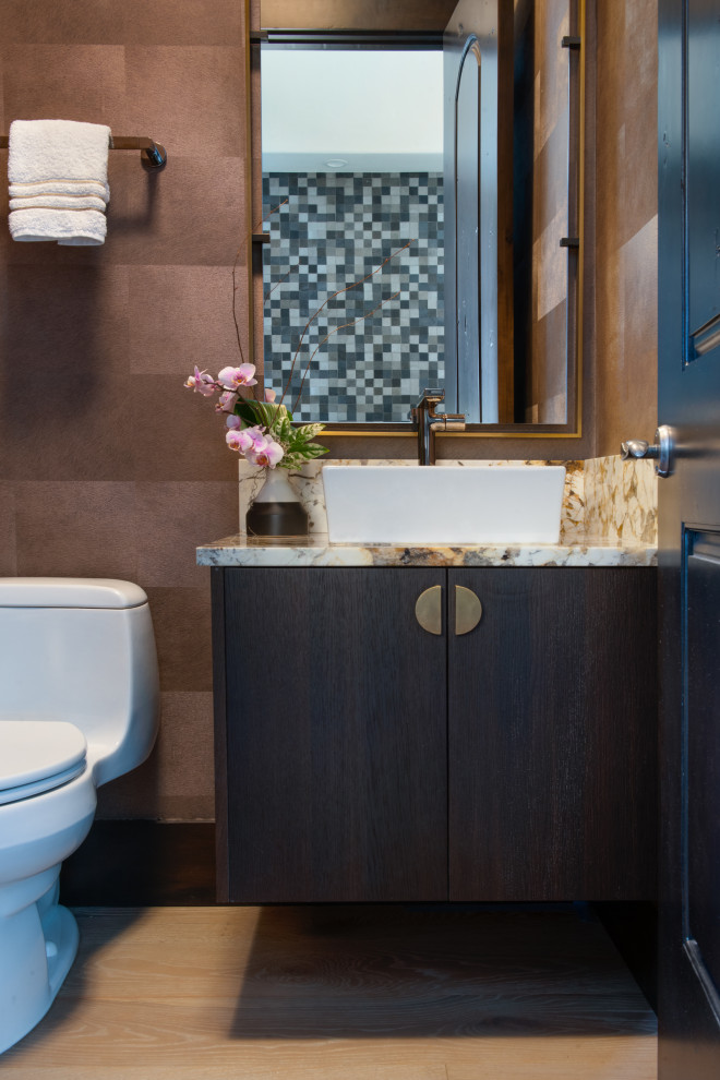Bild på ett litet rustikt vit vitt toalett, med släta luckor, skåp i mörkt trä, en toalettstol med hel cisternkåpa, bruna väggar, mellanmörkt trägolv, ett fristående handfat, granitbänkskiva och brunt golv