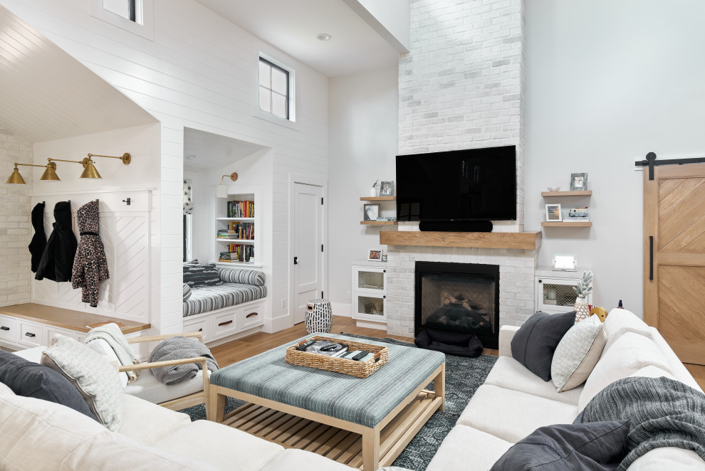 Foto på ett lantligt vardagsrum, med vita väggar, mellanmörkt trägolv, en standard öppen spis, en spiselkrans i tegelsten, en väggmonterad TV och brunt golv