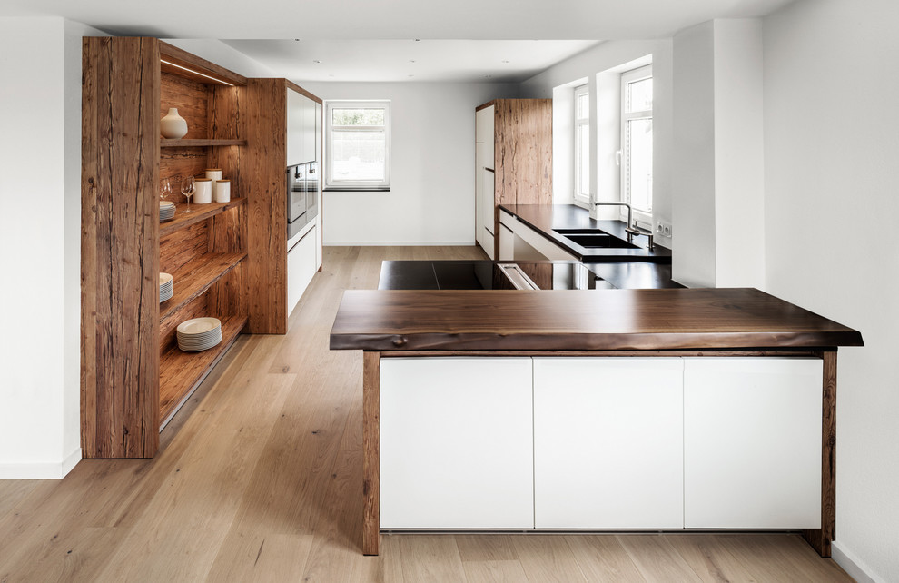 Photo of a large country galley open plan kitchen in Munich with a double-bowl sink, flat-panel cabinets, white cabinets, wood benchtops, medium hardwood floors, a peninsula, white splashback and stainless steel appliances.