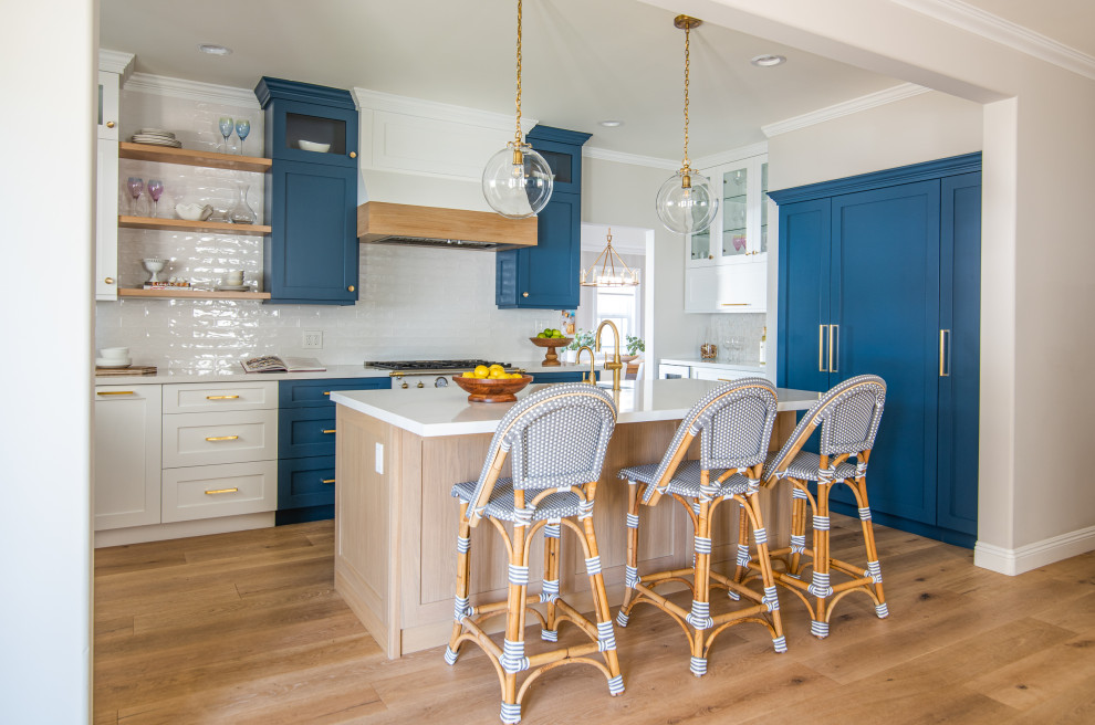 Open concept kitchen - mid-sized coastal u-shaped light wood floor open concept kitchen idea in Los Angeles with a farmhouse sink, shaker cabinets, white cabinets, quartz countertops, white backsplash, subway tile backsplash, an island and white countertops