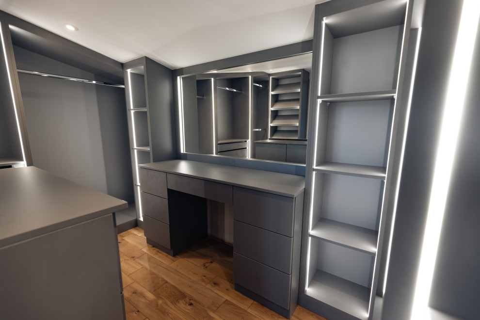 Design ideas for a medium sized contemporary gender neutral dressing room in Buckinghamshire with open cabinets, grey cabinets, light hardwood flooring, brown floors and feature lighting.