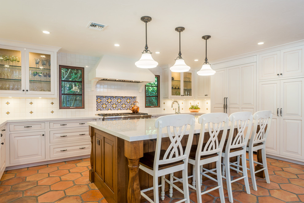 Inspiration for a large mediterranean kitchen in Los Angeles with raised-panel cabinets, white cabinets, marble benchtops, multi-coloured splashback, cement tile splashback, panelled appliances, terra-cotta floors, with island and orange floor.