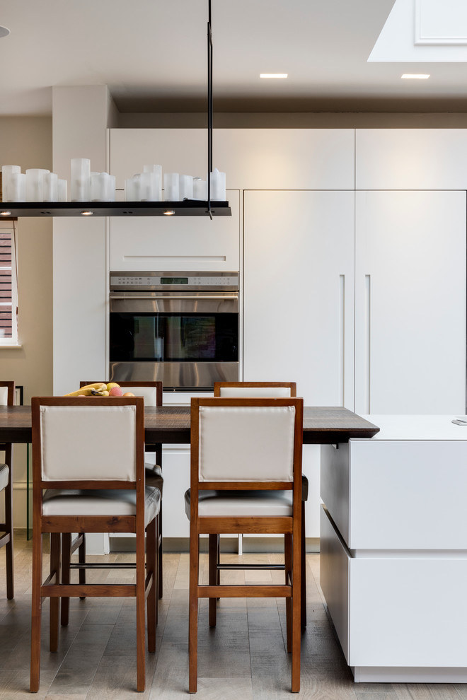 Photo of a large contemporary single-wall open plan kitchen in London with an integrated sink, flat-panel cabinets, white cabinets, solid surface benchtops, stainless steel appliances, ceramic floors and with island.