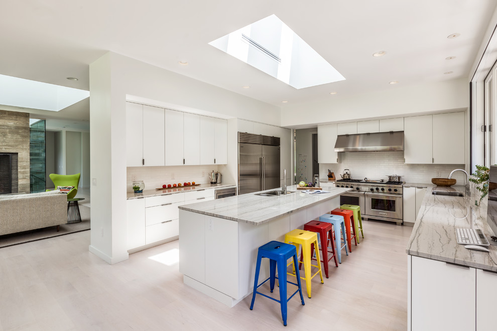 Photo of a large contemporary open plan kitchen in Charleston with an undermount sink, flat-panel cabinets, white cabinets, white splashback, stainless steel appliances, with island and light hardwood floors.