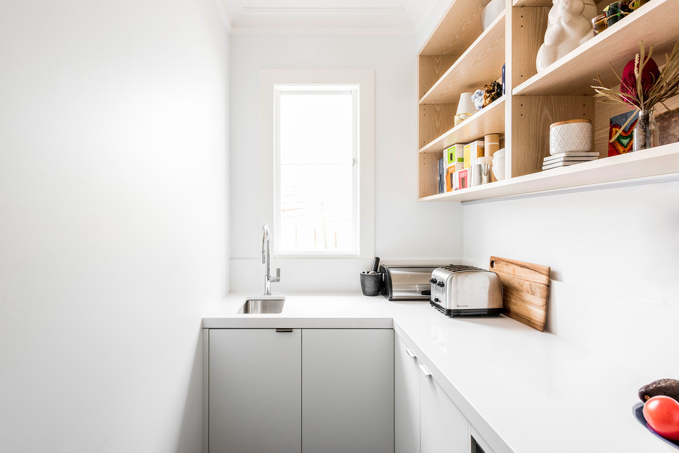 This is an example of a large contemporary l-shaped kitchen pantry in Melbourne with an undermount sink, flat-panel cabinets, white cabinets, quartz benchtops, white splashback, stone slab splashback, black appliances, dark hardwood floors, with island and brown floor.