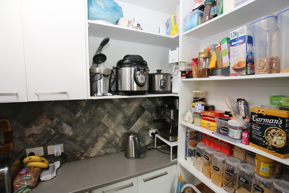 Photo of a large l-shaped kitchen pantry in Sydney with an undermount sink, flat-panel cabinets, white cabinets, tile benchtops, black splashback, mirror splashback, stainless steel appliances, medium hardwood floors and with island.