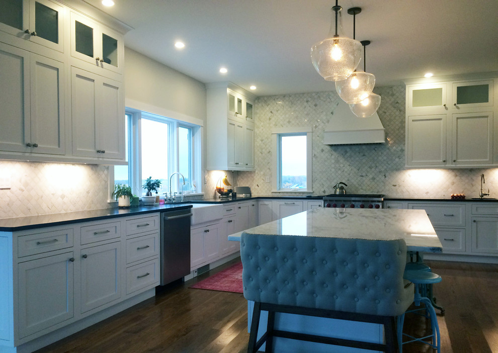 Kitchen pantry - large transitional l-shaped dark wood floor and brown floor kitchen pantry idea with an island, a farmhouse sink, recessed-panel cabinets, white cabinets, quartz countertops, beige backsplash, ceramic backsplash, stainless steel appliances and black countertops