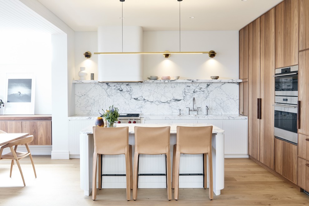 Photo of a contemporary l-shaped kitchen in Sydney with an undermount sink, flat-panel cabinets, white cabinets, white splashback, stone slab splashback, stainless steel appliances, medium hardwood floors, with island, brown floor and white benchtop.