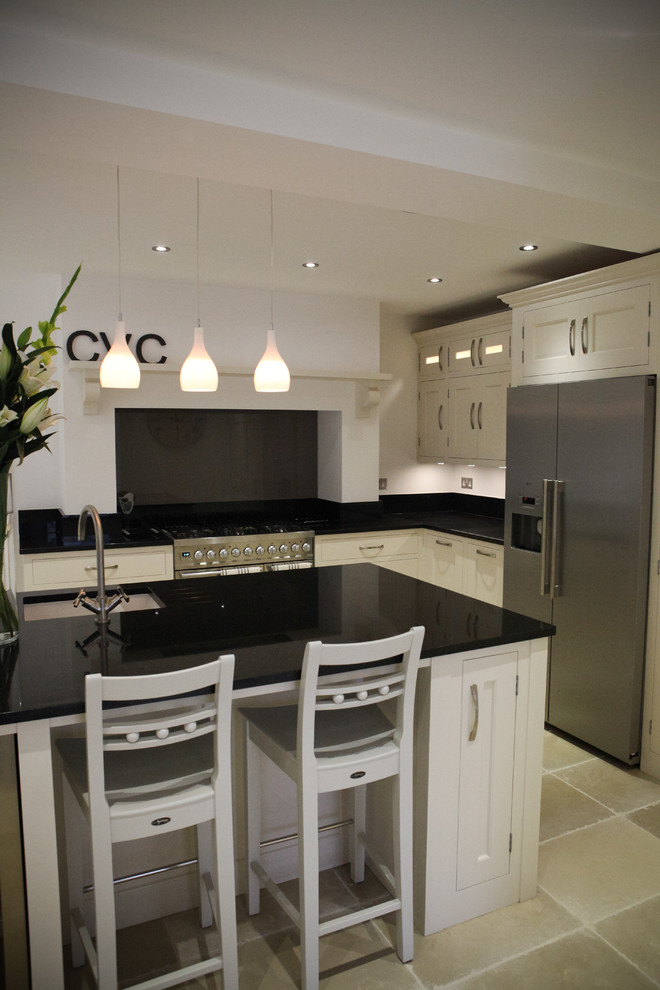 Inspiration for a large traditional l-shaped eat-in kitchen in London with an undermount sink, shaker cabinets, white cabinets, granite benchtops, black splashback, glass sheet splashback, stainless steel appliances, limestone floors and with island.