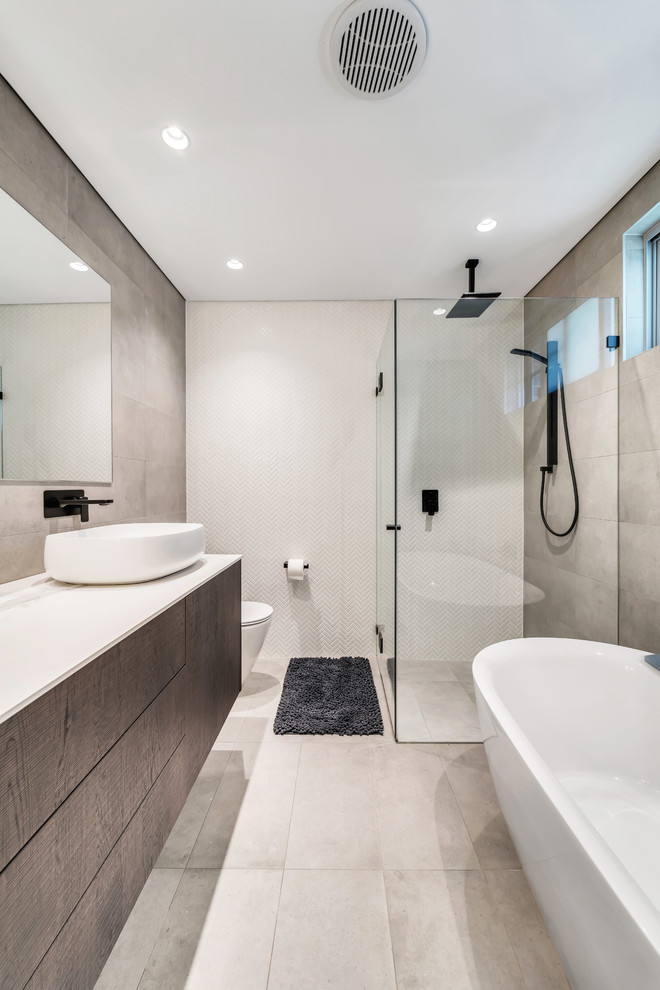 Photo of a mid-sized modern master bathroom in Sydney with flat-panel cabinets, dark wood cabinets, a freestanding tub, a curbless shower, a one-piece toilet, gray tile, ceramic tile, grey walls, ceramic floors, a vessel sink, solid surface benchtops, grey floor, a hinged shower door and grey benchtops.