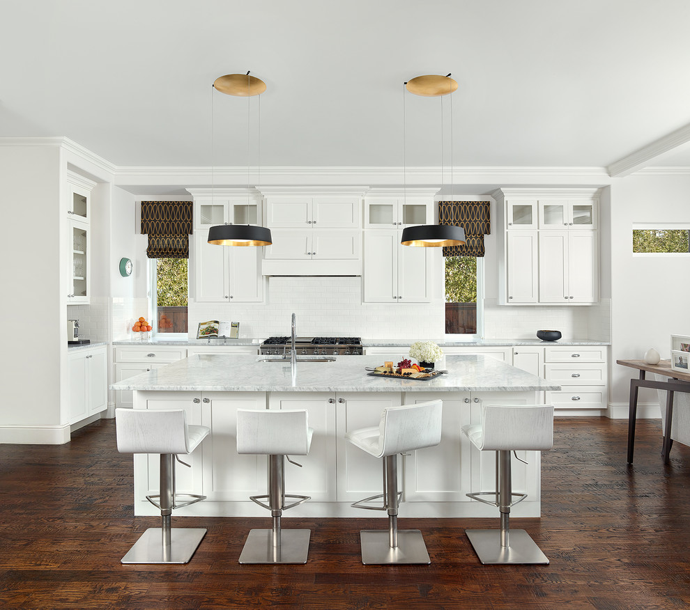 This is an example of a large transitional l-shaped open plan kitchen in Dallas with shaker cabinets, white cabinets, marble benchtops, white splashback, ceramic splashback, stainless steel appliances, dark hardwood floors, with island and an undermount sink.