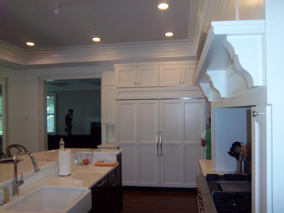Large transitional l-shaped dark wood floor and brown floor eat-in kitchen photo with a farmhouse sink, shaker cabinets, white cabinets, solid surface countertops, white backsplash, stainless steel appliances and an island