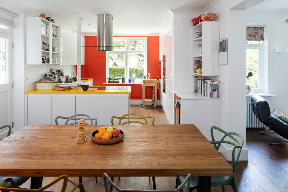 This is an example of a mid-sized eclectic l-shaped eat-in kitchen in London with a drop-in sink, flat-panel cabinets, white cabinets, solid surface benchtops, white splashback, glass sheet splashback, panelled appliances, dark hardwood floors, no island, brown floor and yellow benchtop.