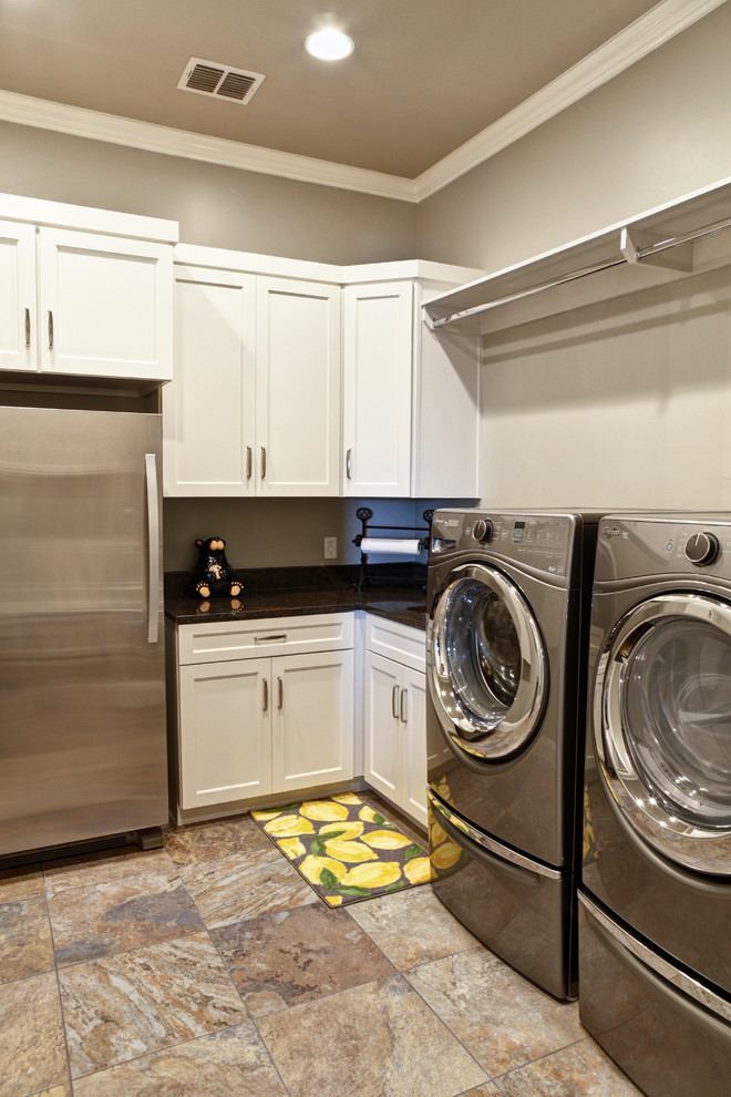 This is an example of a large transitional l-shaped utility room in Austin with shaker cabinets, white cabinets, quartz benchtops, grey walls, porcelain floors, a side-by-side washer and dryer and brown floor.
