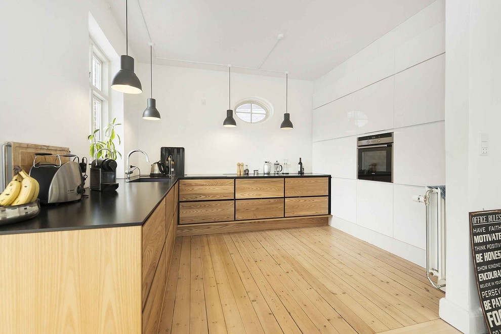 This is an example of a large scandinavian l-shaped separate kitchen in Copenhagen with an undermount sink, flat-panel cabinets, medium wood cabinets, black appliances, medium hardwood floors, laminate benchtops and no island.