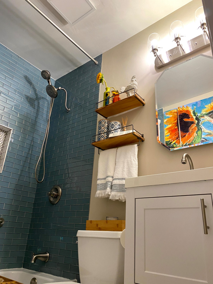 Inredning av ett amerikanskt vit vitt badrum, med öppna hyllor, vita skåp, ett badkar i en alkov, en dusch/badkar-kombination, en toalettstol med separat cisternkåpa, blå kakel, beige väggar, ett nedsänkt handfat, vitt golv och dusch med duschdraperi