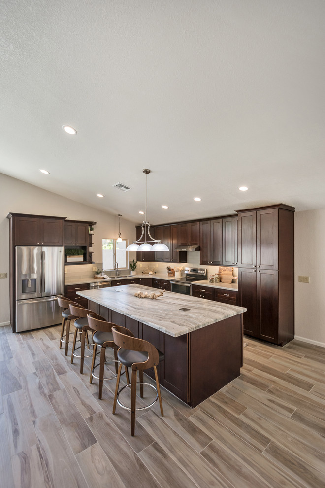 Inspiration for a mid-sized transitional l-shaped open plan kitchen in Phoenix with an undermount sink, shaker cabinets, brown cabinets, granite benchtops, grey splashback, glass tile splashback, stainless steel appliances, porcelain floors, with island, brown floor and multi-coloured benchtop.