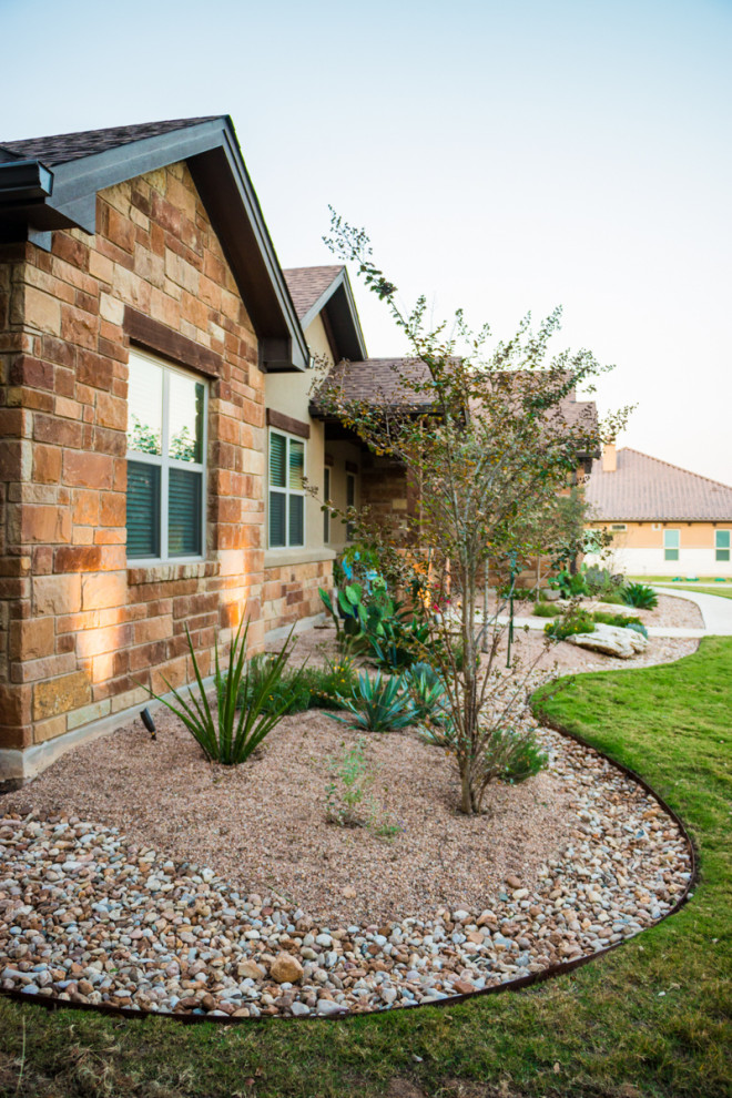 Inspiration for a mid-sized and desert look traditional front yard full sun xeriscape for summer in Austin with river rock.