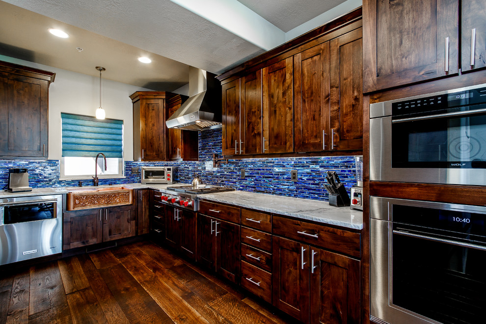 Mid-sized arts and crafts l-shaped eat-in kitchen in Salt Lake City with a farmhouse sink, recessed-panel cabinets, dark wood cabinets, granite benchtops, blue splashback, stone tile splashback, stainless steel appliances, dark hardwood floors, no island and brown floor.