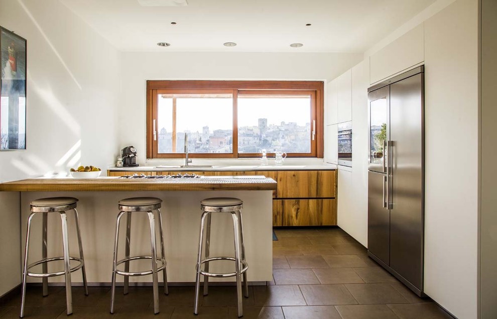 Photo of a contemporary u-shaped kitchen in Other with flat-panel cabinets, stainless steel appliances, grey floor, medium wood cabinets, wood benchtops, a peninsula and brown benchtop.