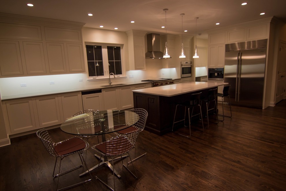Mid-sized transitional l-shaped dark wood floor enclosed kitchen photo in Chicago with an undermount sink, recessed-panel cabinets, white cabinets, solid surface countertops, white backsplash, porcelain backsplash, stainless steel appliances and an island