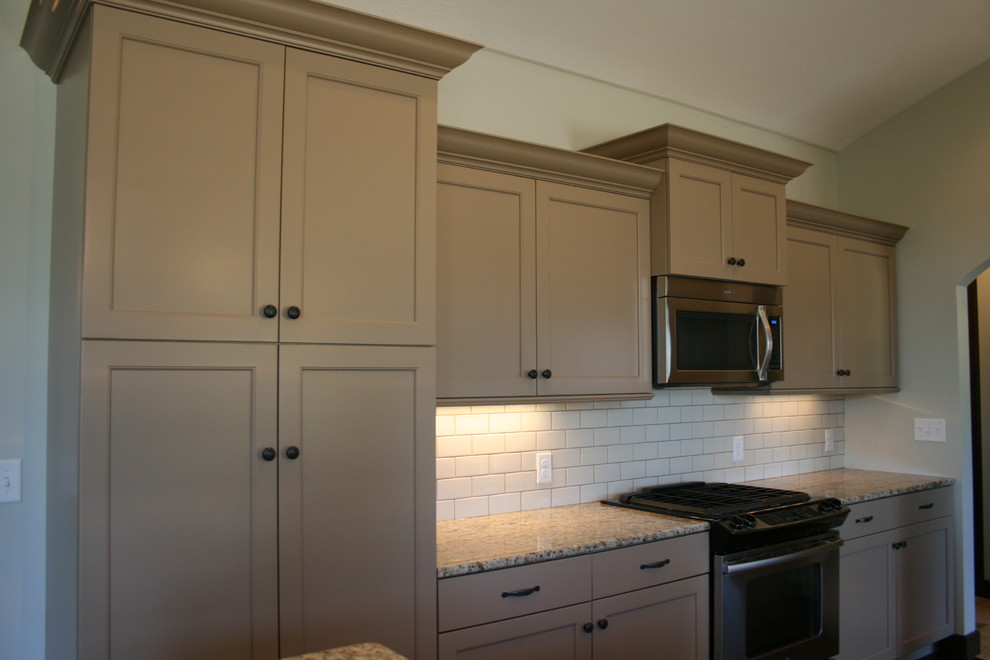 Mid-sized mountain style dark wood floor kitchen photo in Omaha with an undermount sink, shaker cabinets, beige cabinets, granite countertops, white backsplash, subway tile backsplash, stainless steel appliances and an island
