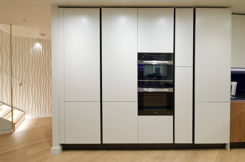 Design ideas for a large modern l-shaped open plan kitchen in London with a drop-in sink, flat-panel cabinets, white cabinets, quartzite benchtops, black splashback, black appliances, a peninsula and black benchtop.