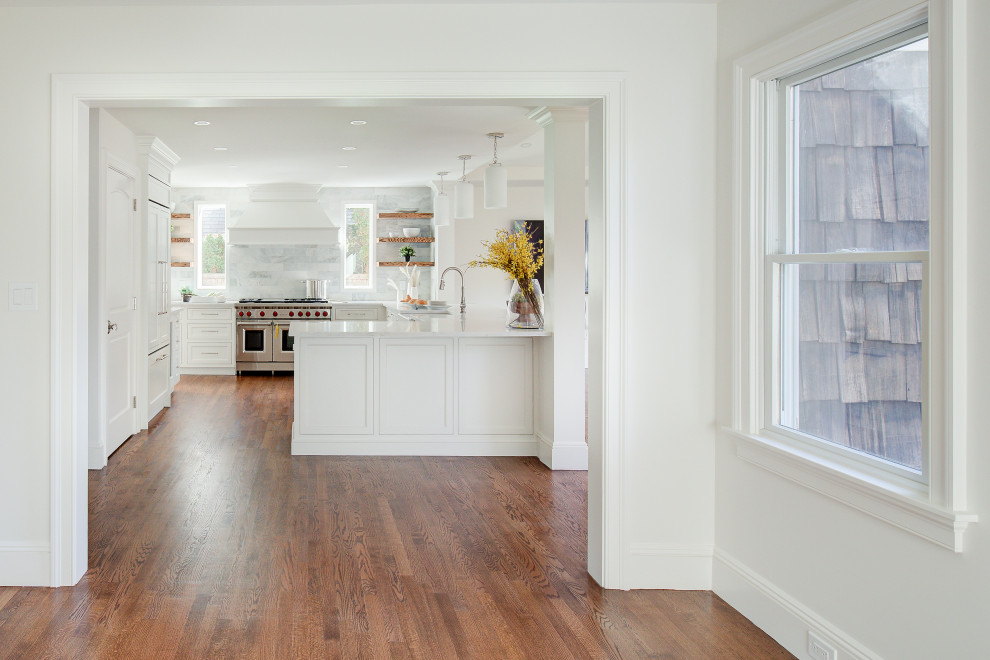 Example of a mid-sized transitional u-shaped medium tone wood floor and brown floor open concept kitchen design with a farmhouse sink, recessed-panel cabinets, white cabinets, quartz countertops, multicolored backsplash, marble backsplash, stainless steel appliances, a peninsula and white countertops