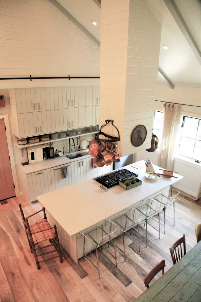 サンタバーバラにあるカントリー風のおしゃれなキッチン (白いキャビネット、シルバーの調理設備、淡色無垢フローリング、白いキッチンカウンター、三角天井) の写真