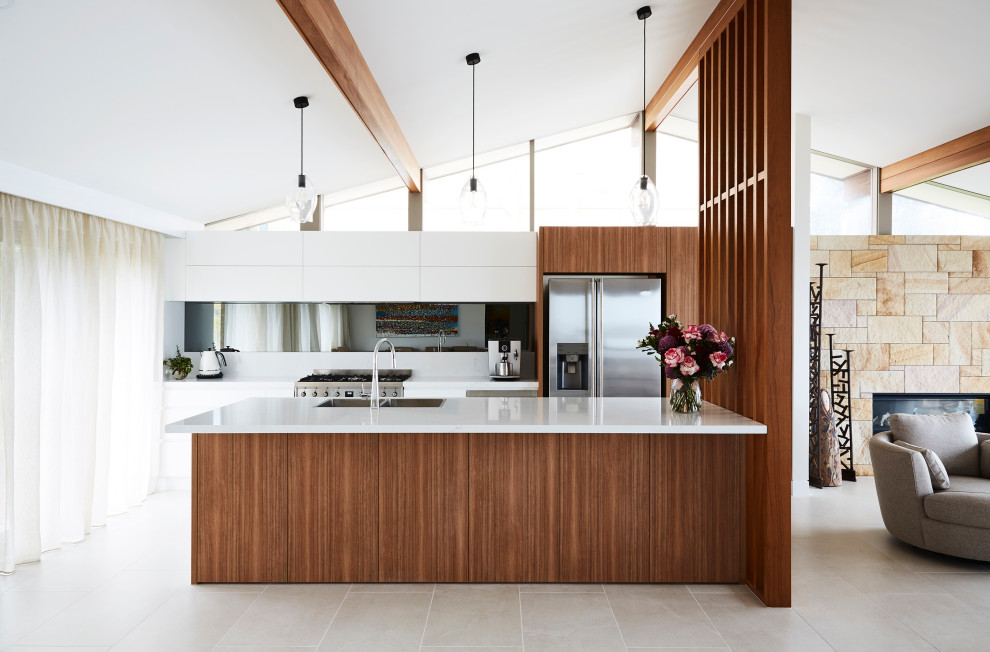 Photo of a mid-sized contemporary galley open plan kitchen in Sydney with a double-bowl sink, flat-panel cabinets, white cabinets, quartz benchtops, grey splashback, mirror splashback, stainless steel appliances, ceramic floors, with island, grey floor and white benchtop.
