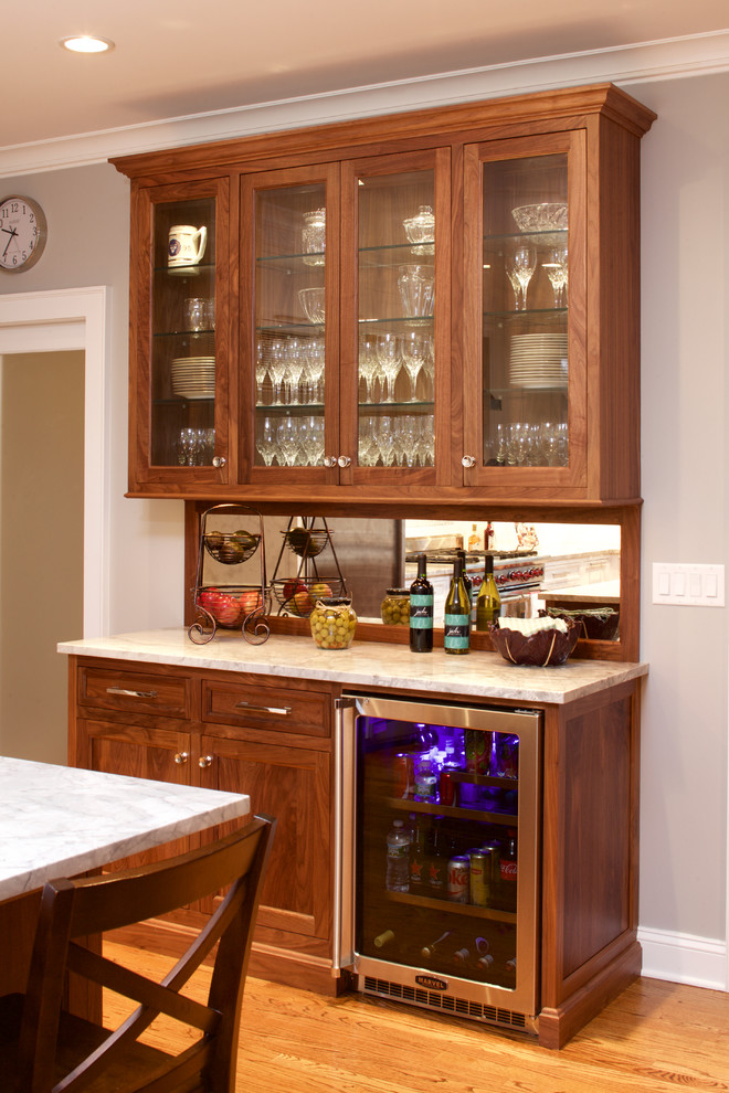 Large transitional u-shaped light wood floor kitchen photo in New York with recessed-panel cabinets, medium tone wood cabinets, marble countertops, mirror backsplash, stainless steel appliances and an island