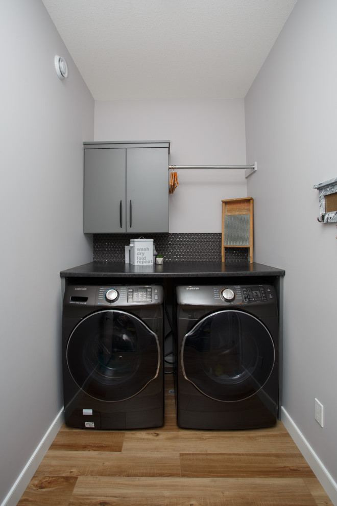 Design ideas for a small modern single-wall dedicated laundry room in Calgary with flat-panel cabinets, grey cabinets, laminate benchtops, black splashback, mosaic tile splashback, grey walls, laminate floors, a side-by-side washer and dryer, blue floor and black benchtop.