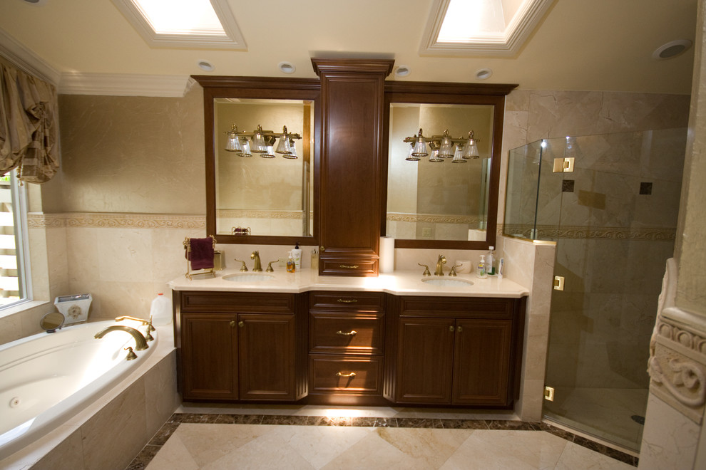 Design ideas for a tropical master bathroom in Miami with raised-panel cabinets, dark wood cabinets, a drop-in tub, a corner shower, beige tile, stone tile, beige walls, marble floors, an undermount sink, solid surface benchtops, beige floor and a hinged shower door.