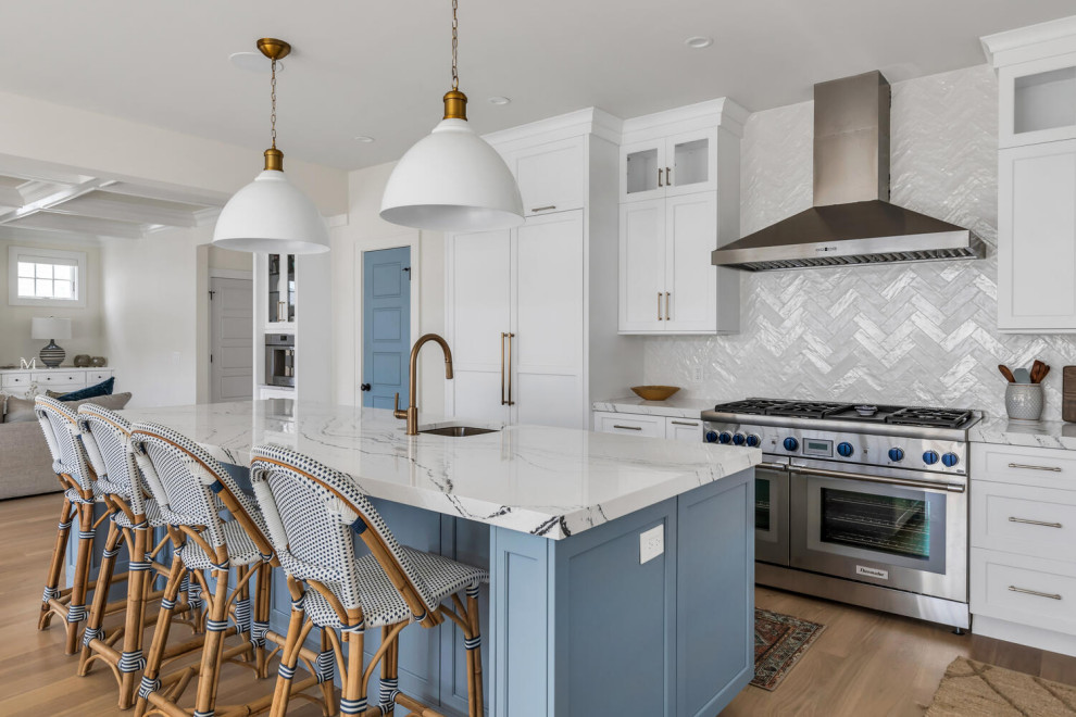 Photo of a mid-sized beach style l-shaped open plan kitchen in New York with an undermount sink, flat-panel cabinets, white cabinets, quartz benchtops, grey splashback, panelled appliances, medium hardwood floors, with island, brown floor and white benchtop.