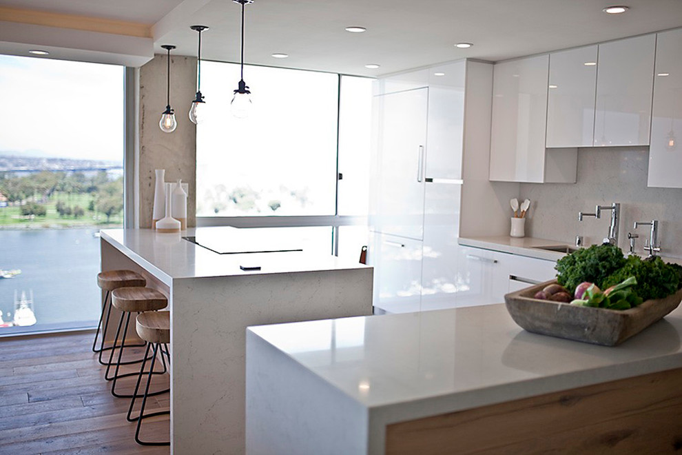 Photo of a mid-sized contemporary l-shaped eat-in kitchen in San Diego with an undermount sink, flat-panel cabinets, white cabinets, quartz benchtops, grey splashback, stone slab splashback, panelled appliances, light hardwood floors and with island.